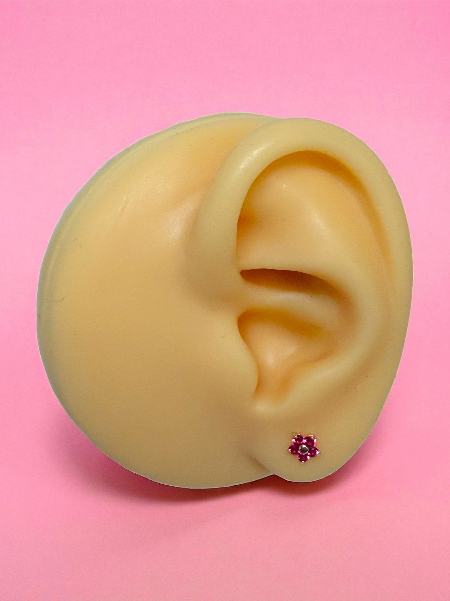 Realistic silicone ear with a 14K Gold Flower Earring with ruby pink cz petals on a pink background