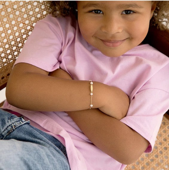 little girl relaxing in a chair with arms folded showing a 14k gold and white pearl bracelet on her arm