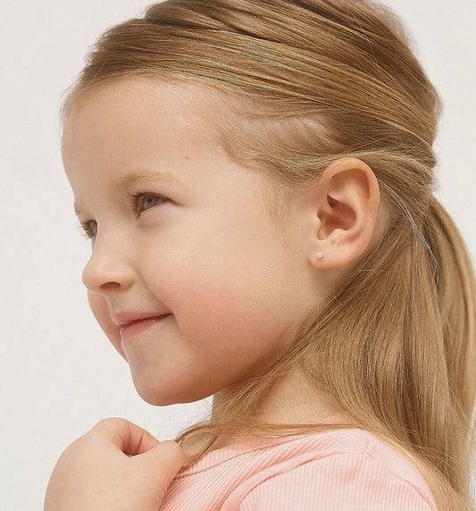 A young girl with blonde hair tied back to reveal the small white pearl earrings in her ears