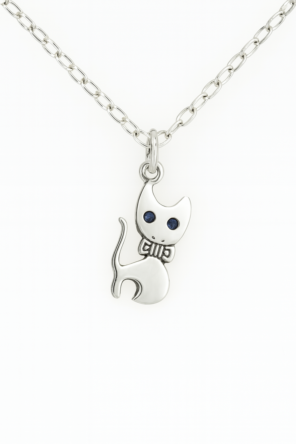 Product image of a silver cat pendant necklace with a stylized design, featuring indented black eyes and a bowtie detail. The pendant hangs from a silver chain with oval links, displayed against a plain white background.