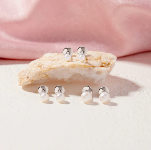 Pearl earrings displayed on a shell with a soft pink background