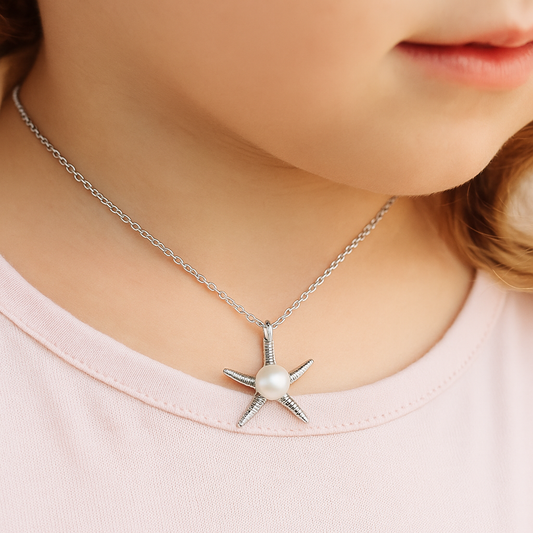 Close-up of a young girl wearing a sterling silver starfish pendant necklace with a centred pearl, shown against a softly blurred background.