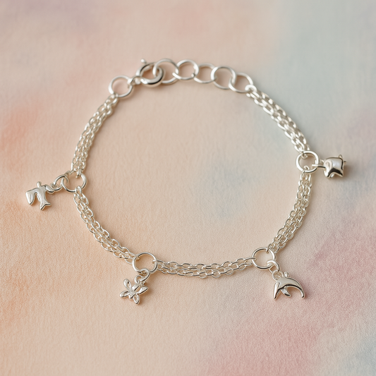 Sterling silver children’s charm bracelet with double chains and four small animal charms—a hummingbird, butterfly, dolphin, and elephant—laid out on a soft pastel watercolour background.