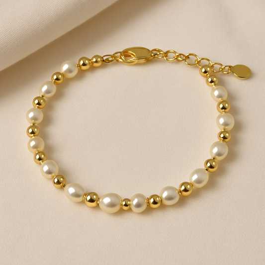 Children’s bracelet with alternating freshwater pearls and shiny gold beads, featuring a gold lobster clasp and heart charm, displayed on a soft beige fabric background