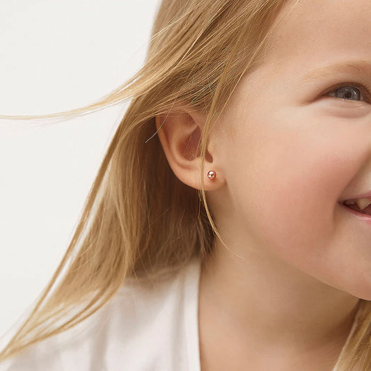 A smiling child wearing 14k solid rose gold ball stud screw back children's earrings, showcasing timeless elegance.