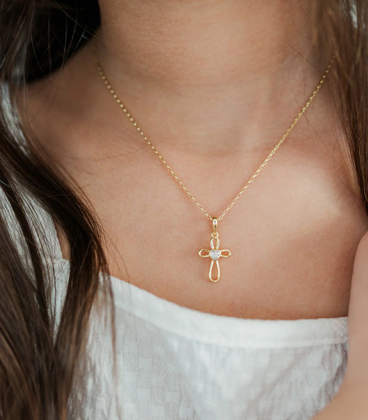 Gold necklace with a cross pendant on a person wearing a white top.