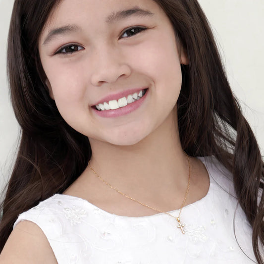 Young girl with a smile wearing a white top and gold necklace on a plain background