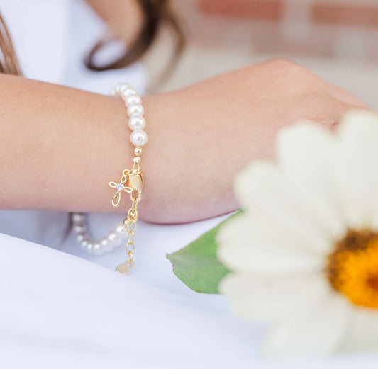 Children's bracelets featuring Swarovski® simulated pearls and a gold-plated infinity loop cross charm.