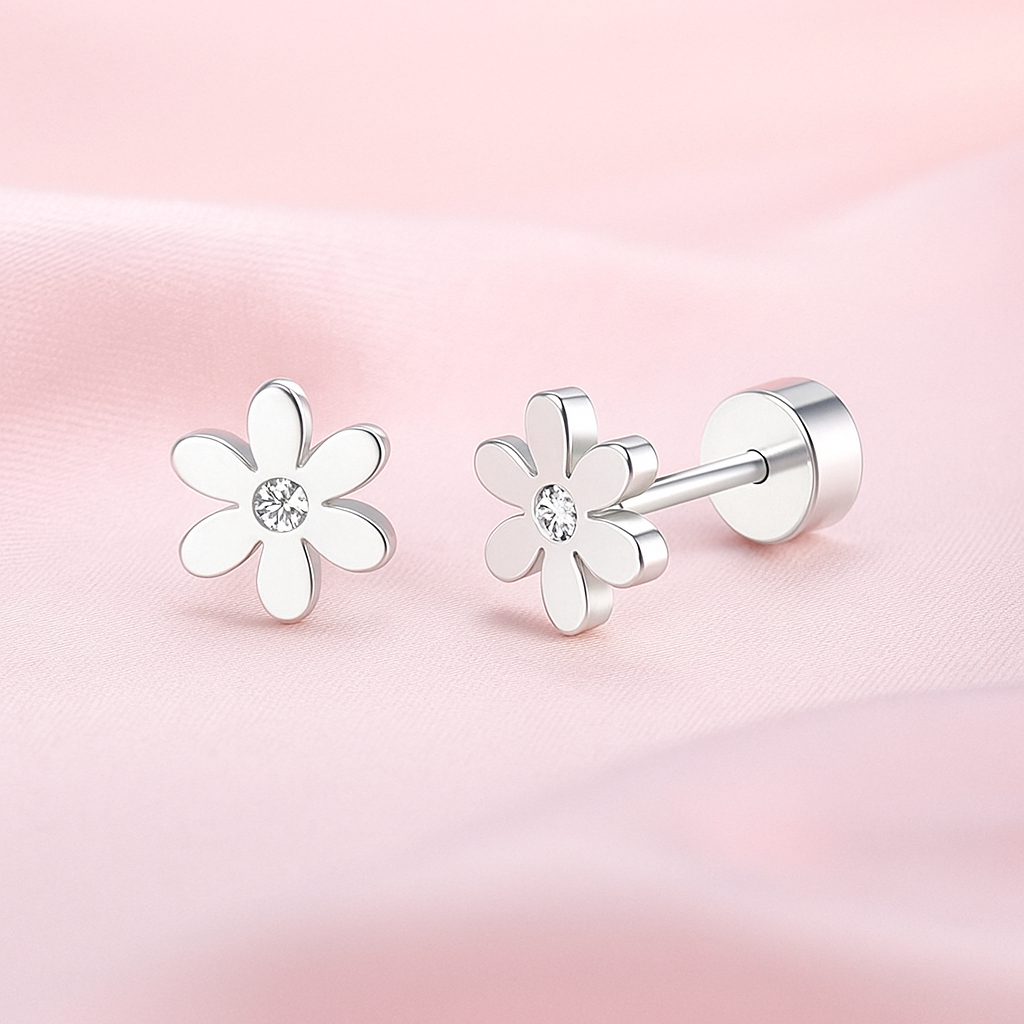 A pair of stainless steel children's flower stud earrings with clear cubic zirconia centres, shown on a soft pink fabric