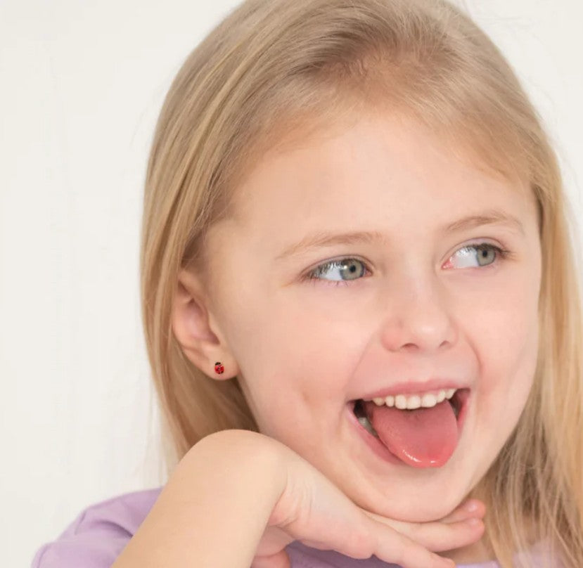 A smiling girl wearing ladybug earrings, showcasing her playful personality with a cute expression.