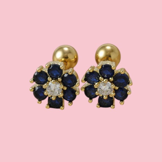 Gold earrings with blue flower-shaped stones on a pink background