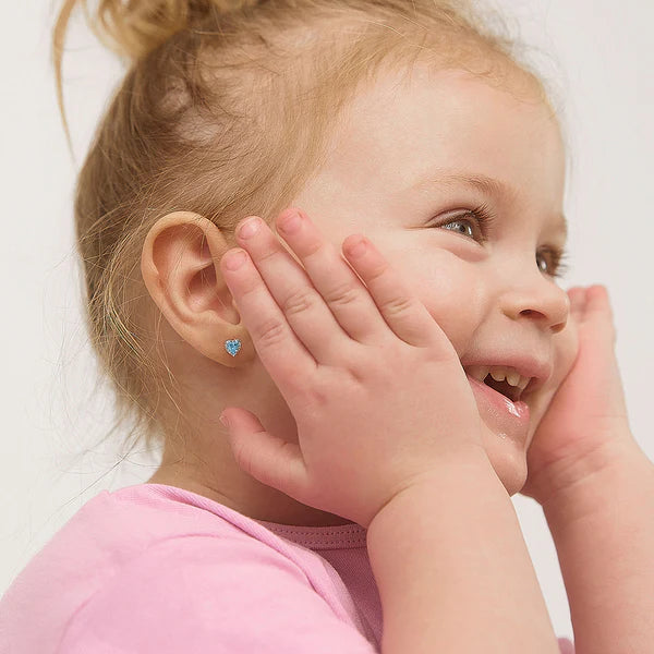 Child wearing a blue heart-shaped earring on a plain background