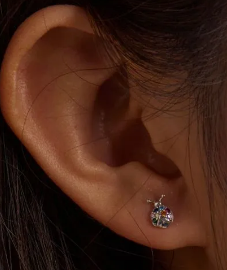 Close-up of a child's ear wearing a small sterling silver ladybug stud earring with colourful gemstones.