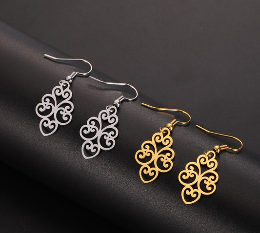 two pairs of hook earrings with intricate scrolling patterns (one gold and one silver coloured) against a dark surface