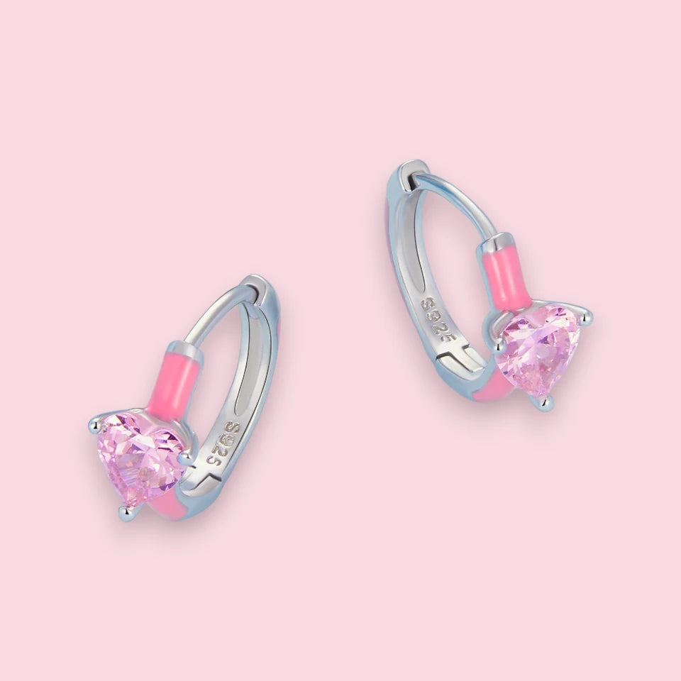 Heart hoop earrings featuring pink enamel and sparkling cubic zirconia hearts on a pastel background.