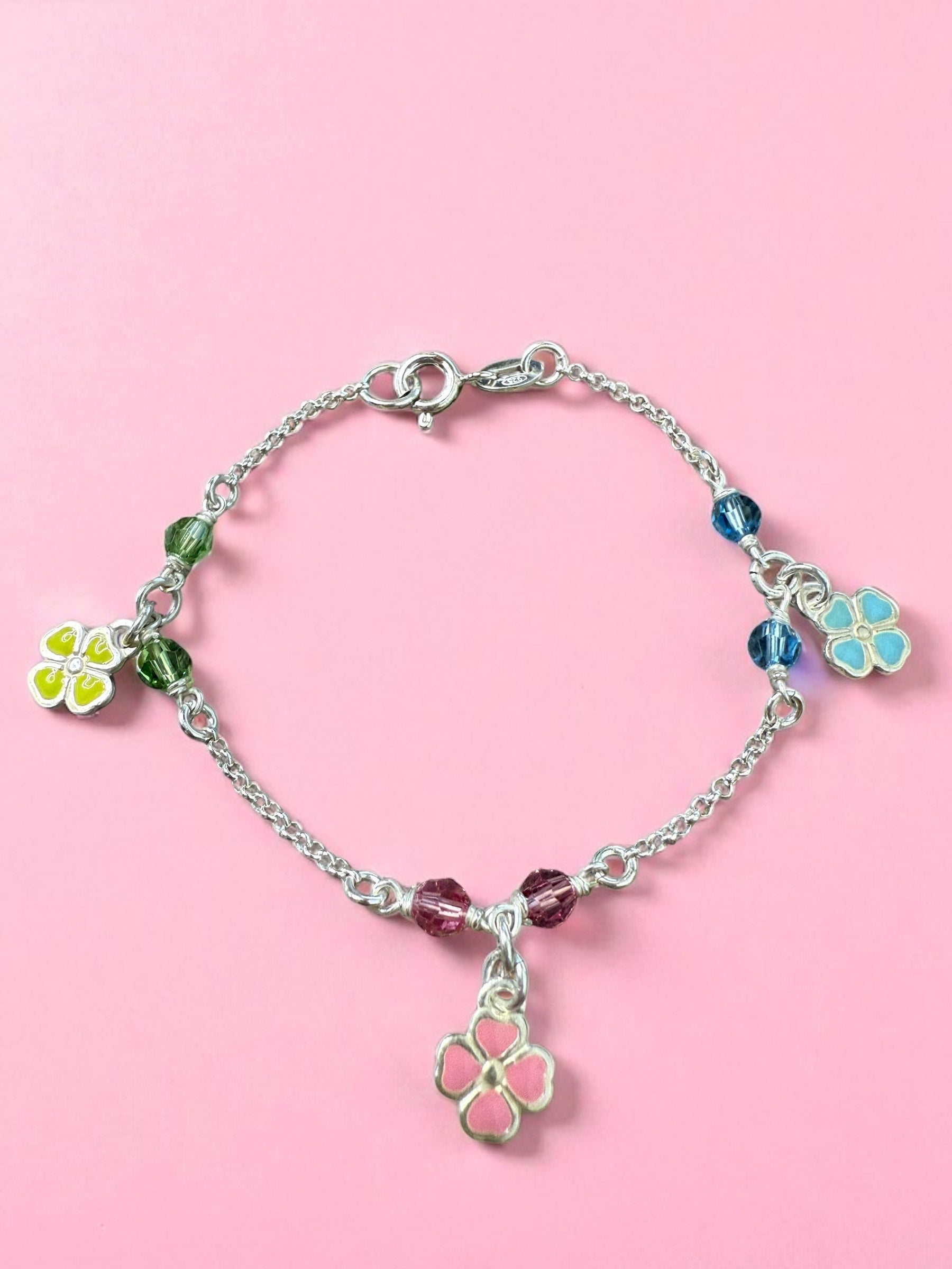 Silver bracelet with colorful flower charms on a pink background