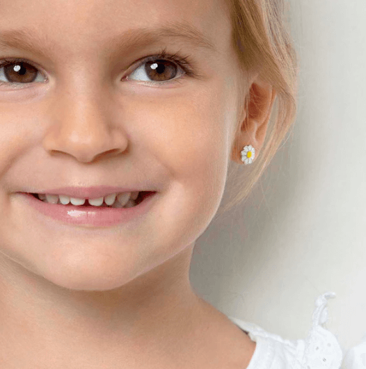 Close-up of a young girl wearing a daisy flower earring on a plain background