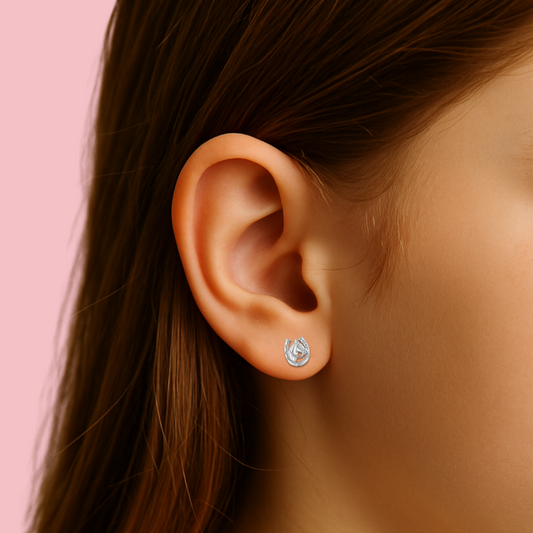 Close-up of an ear wearing a diamond stud earring with a pink background