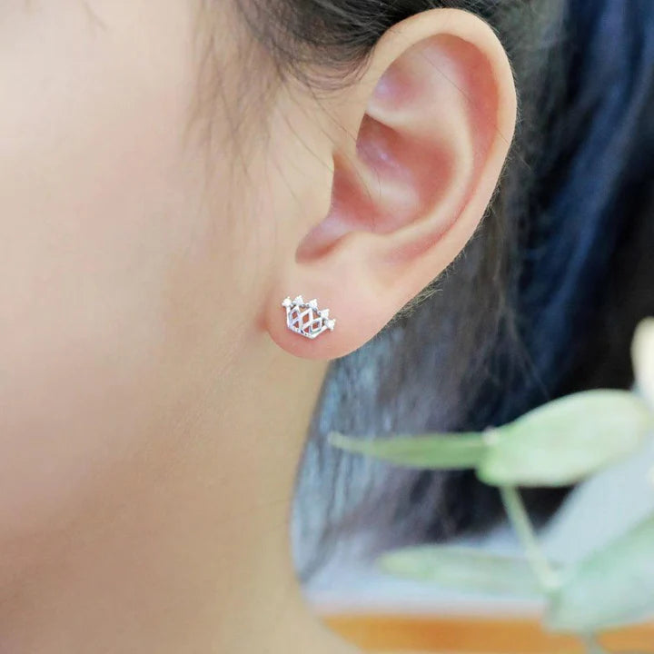 A close up photo of sterling silver crown studs with cubic zirconia accents in a little girl's ear