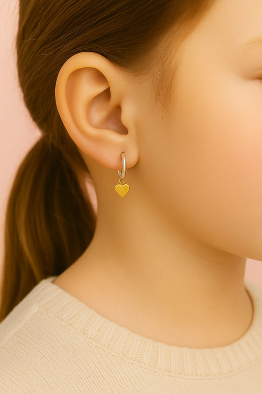 Close-up of an ear wearing a gold heart-shaped earring against a pink background