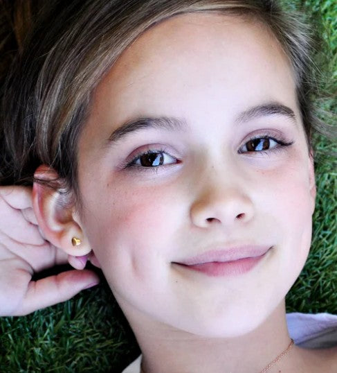 Heart earrings on a smiling girl laying on grass, showcasing the gold plated heart design and secure screw backs.