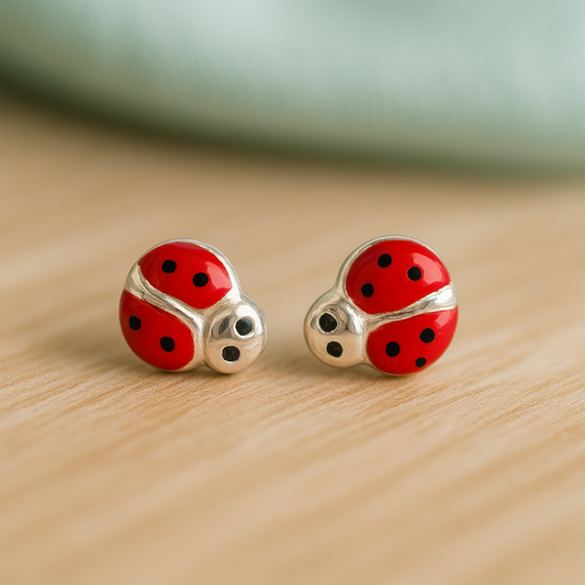 silver ladybug earrings with red and black enamel wings on a blurred soft wood background