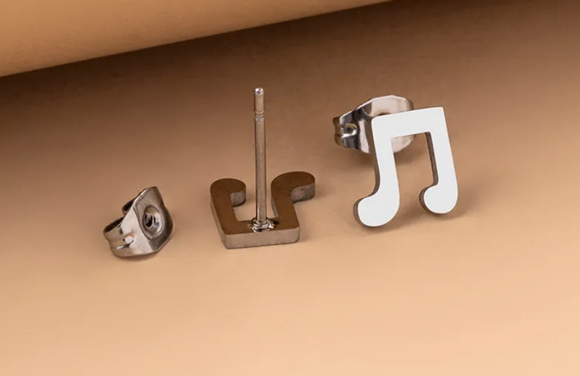 Pair of stainless steel musical note stud earrings displayed on a soft, light lifestyle background.