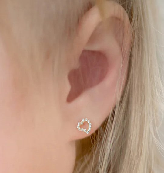 Close up image of a child's ear showcasing a 14k gold open heart design earring paved with clear cubic zirconia