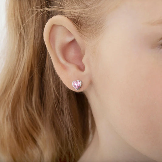 close up lifestyle image of a young girl's ear wearing heart shaped sterling silver stud earrings with pink cubic zirconia on a softly blurred background