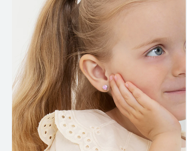 close up lifestyle image of a young girl's ear wearing heart shaped sterling silver stud earrings with pink cubic zirconia on a softly blurred background