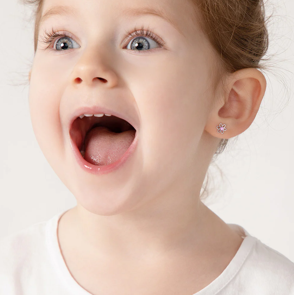 A little girl with an excited expression on her face wearing silver flower earrings on her ears with pink cz centres