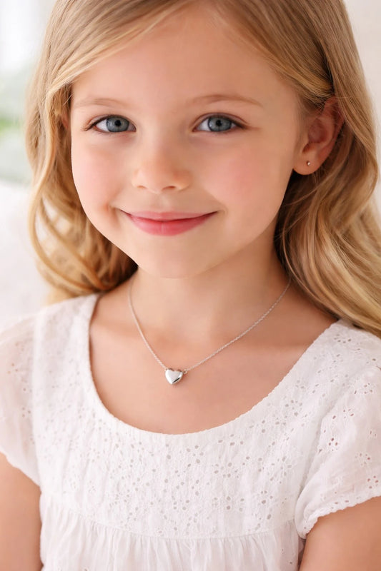 A young girl smiling while wearing a children's necklace featuring a polished surgical steel puffy heart design.