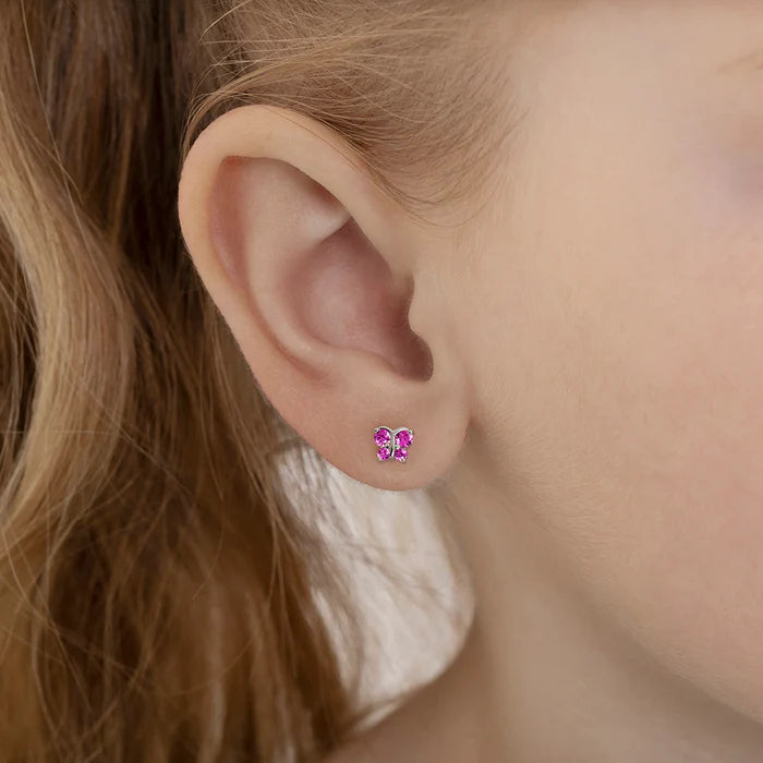 Close up picture of silver butterfly shaped studs with ruby coloured cubic zirconia wings in the ear of a little girl