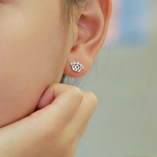 A close up photo of sterling silver crown studs with cubic zirconia accents in a little girl's ear