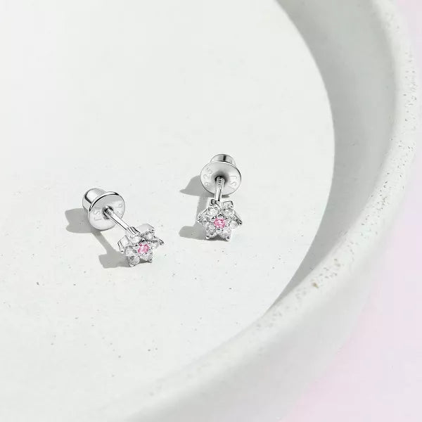 A pair of sterling silver children's earrings featuring a flower design with white and pink cubic zirconia in a white bowl