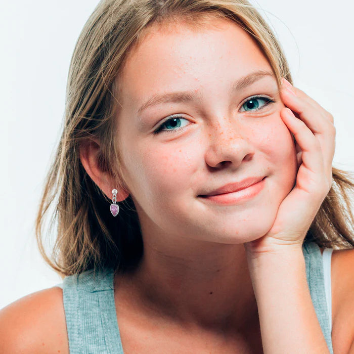 A young blonde girl with silver ball stud earrings with dangling pink cubic zirconia heart charms in her ears