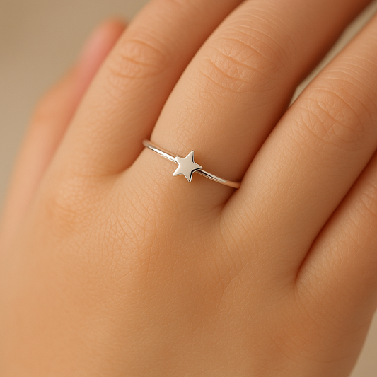 Close-up of a child’s left hand with soft, smooth skin wearing a thin sterling silver ring topped with a small, polished five‑pointed star, set against a softly blurred beige background.