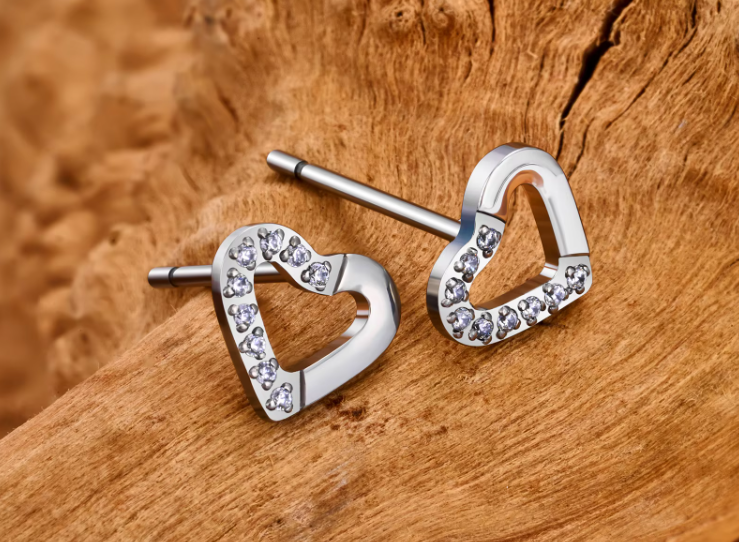 Heart-shaped silver earrings with embedded stones on a wooden surface