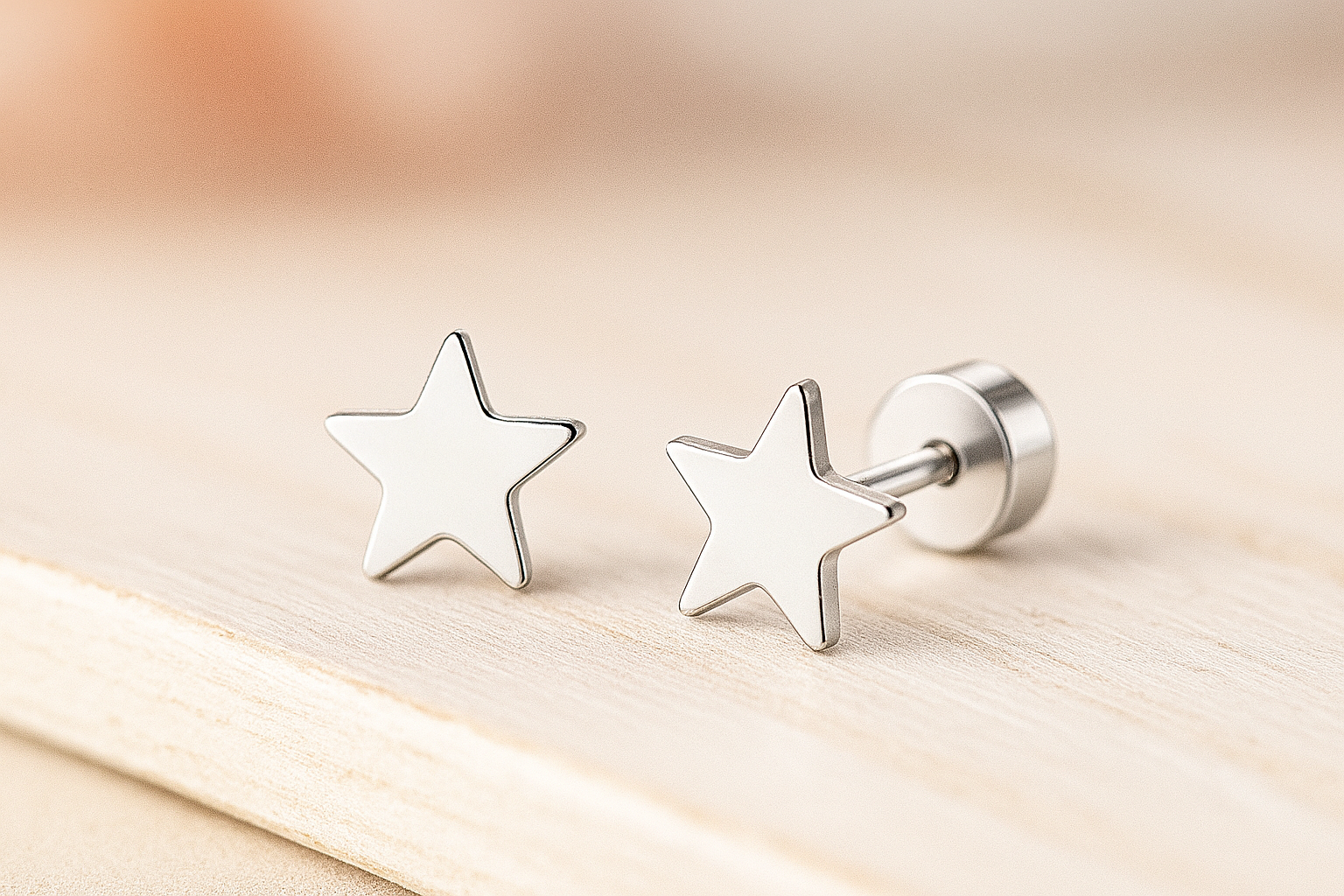 A pair of children's stainless steel star-shaped stud earrings displayed on a light wooden surface with a soft, warm background