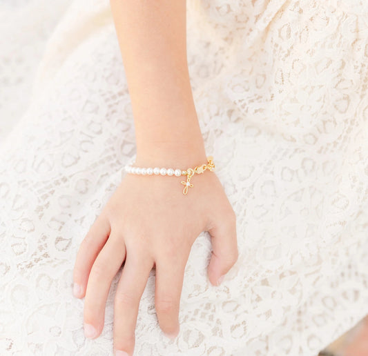 Children's bracelets with Swarovski® simulated pearls on a child's wrist, featuring an elegant gold-plated cross for christening.