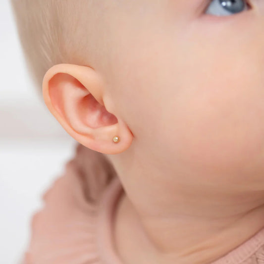Close-up of a baby's ear with solid 14k yellow gold ball stud baby earrings, showcasing elegant and safe design.