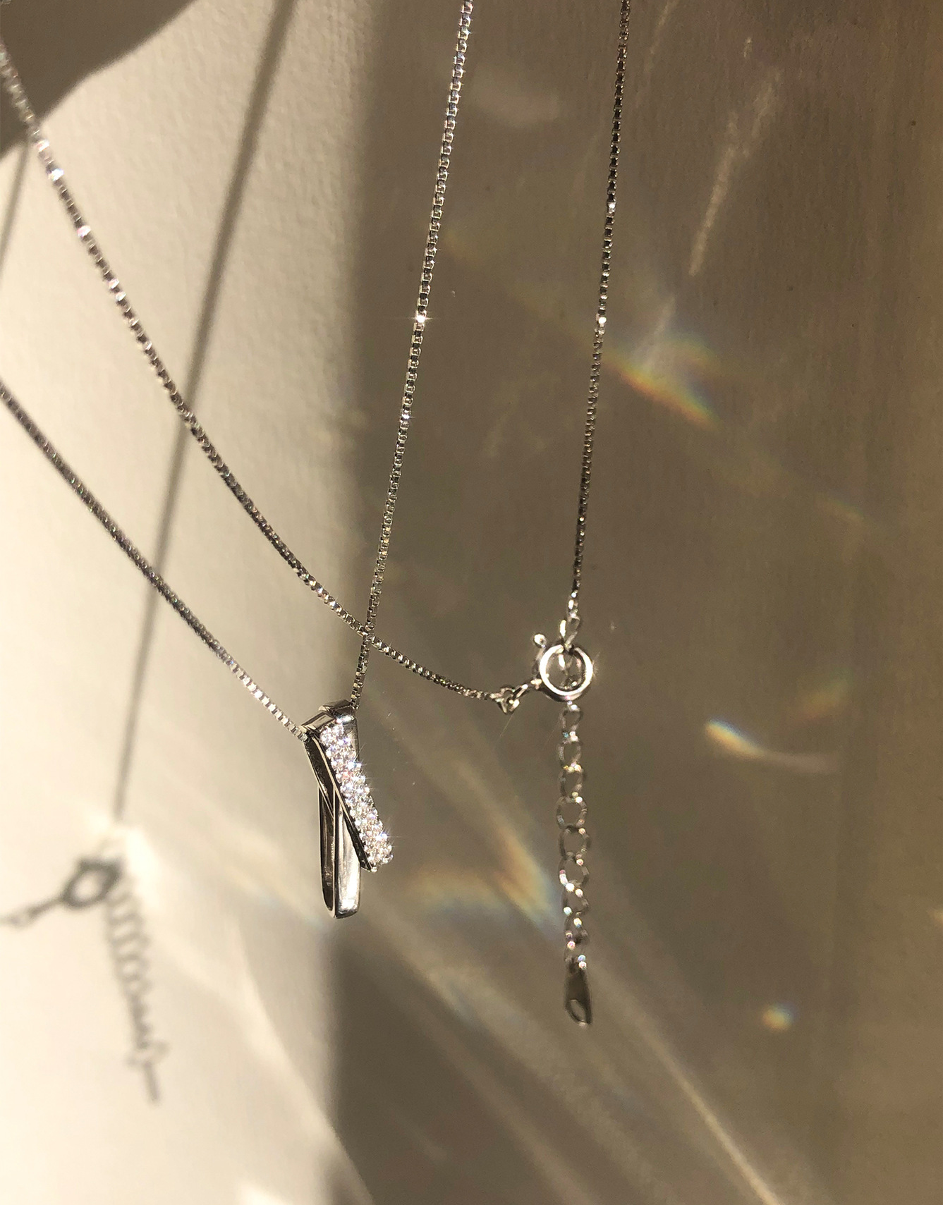 Sterling silver criss-cross bar pendant necklace hanging outside in the sunlight casting rainbows with its sparkling cubic zirconia