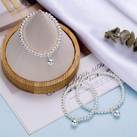 Baby bracelets featuring sterling silver ball design and charm, elegantly displayed on a wooden stand.