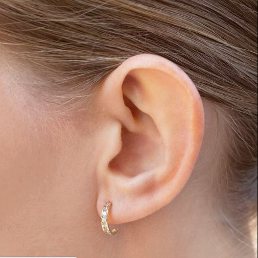 Close-up of a child's ear wearing elegant 14k solid gold children's earrings with clear CZ accents.