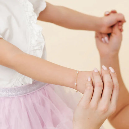 14k gold baby bracelet on a child's wrist, showcasing elegant design with pearls, perfect for special moments.
