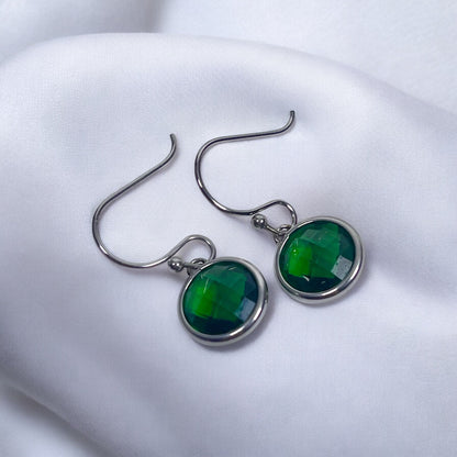 Hook earrings featuring 10mm faceted emerald cubic zirconia set in titanium, nestled on a soft fabric.