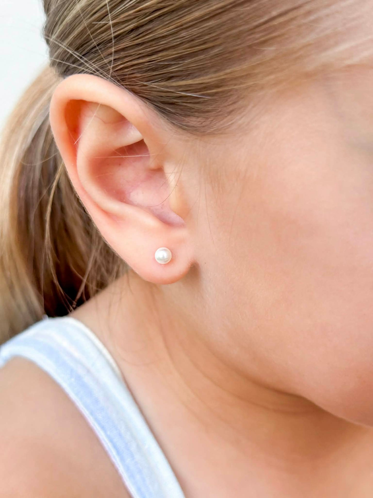Pearl earrings showcased on a young girl, featuring 4mm simulated pearls in 14k gold over sterling silver settings.