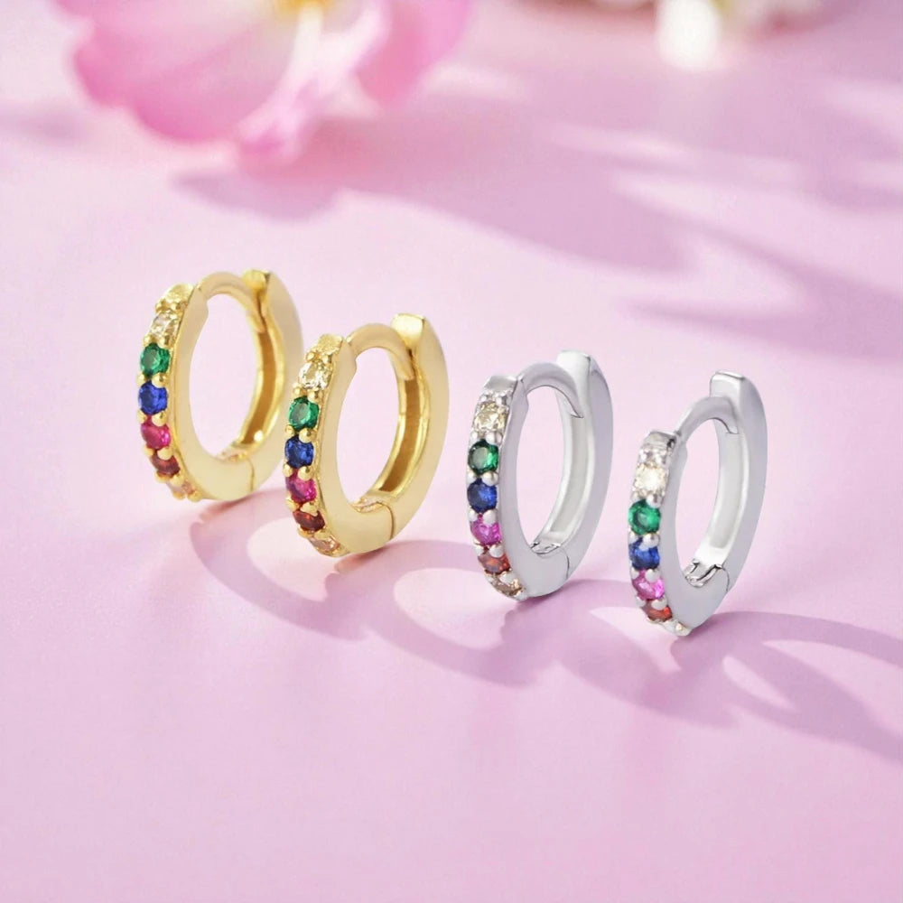 Baby hoop earrings in 925 sterling silver with colorful rainbow CZ huggie hoops on a pink background.