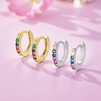 Baby hoop earrings in 925 sterling silver with colorful rainbow CZ huggie hoops on a pink background.