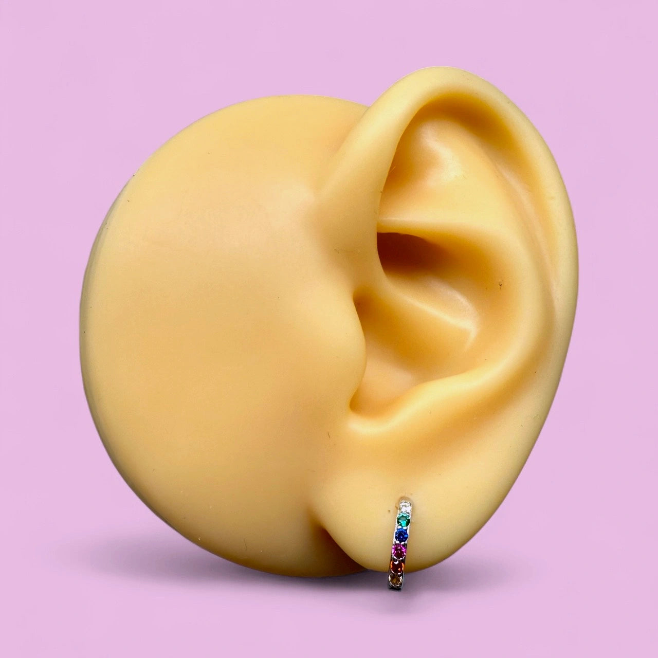 Baby hoop earrings displayed on a realistic ear model showcasing colorful rainbow CZ design.